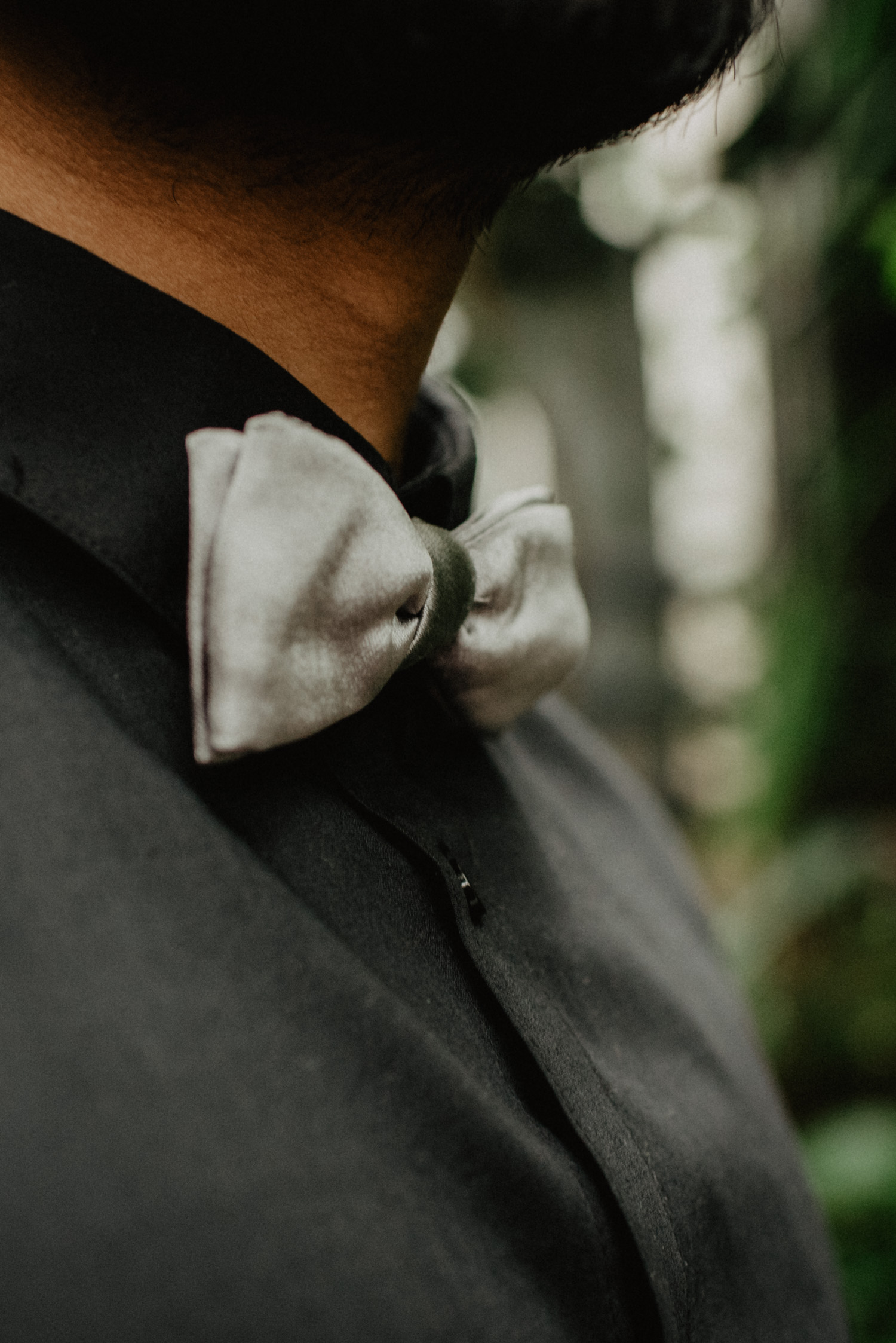 Detailfoto des Bräutigams. Es ist ein schwarzes Hemd mit einer grauen Fliege zu sehen.