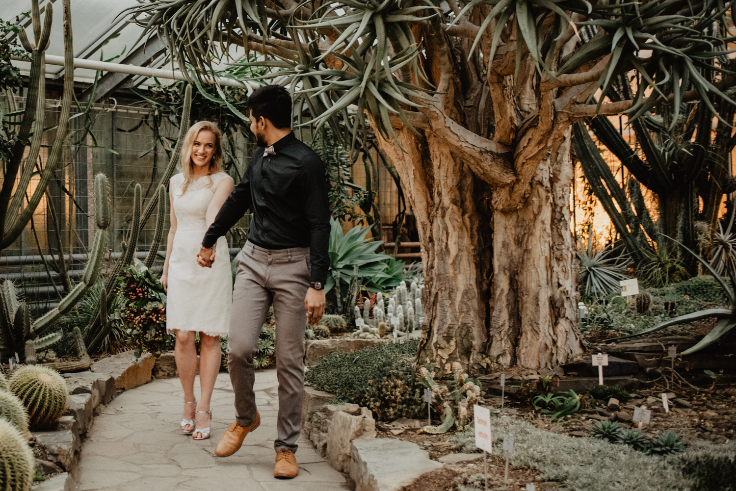 Ein Brautpaar spaziert beim Hochzeits-Fotoshooting umgeben von Wüstenpflanzen.