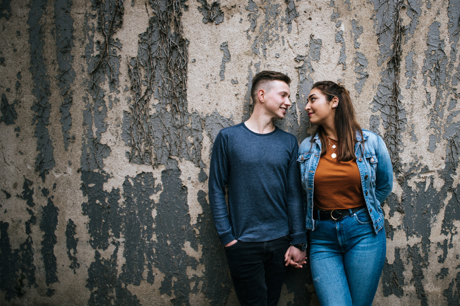 Love Story Shootin in Bonn, ein Paar schaut sich verliebt an während es an einer alten bewachsenen Wand steht.