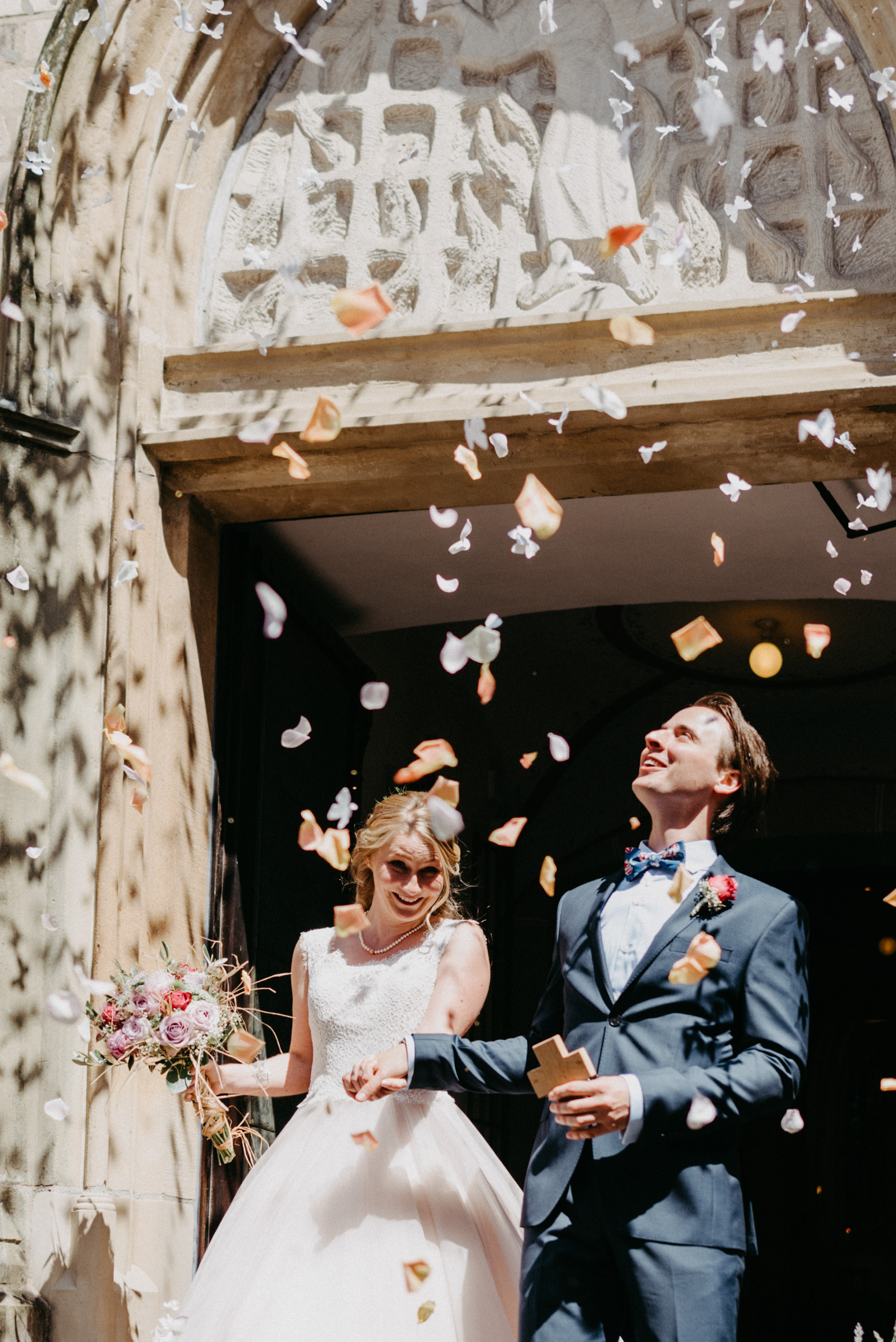 Auszug des Brautpaares aus der Kirche. Fliegendes Konfetti. Hochzeitsfotografin Daria Becker von Genuine Bonds aus Bonn