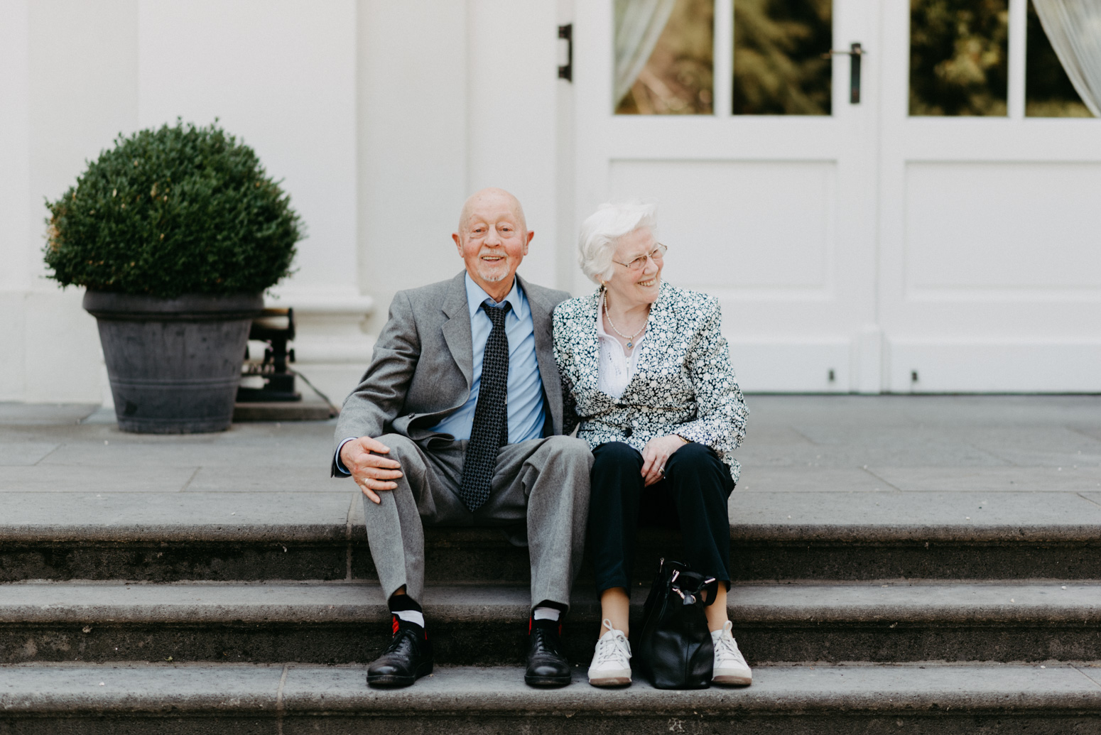 Älteres Paar sitzt Arm in Arm auf einer Treppe. 